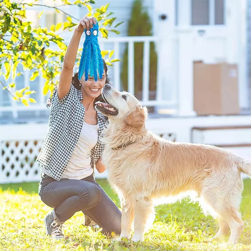 A woman playing fetch outdoors with a happy golden retriever dog using a blue octopus toy